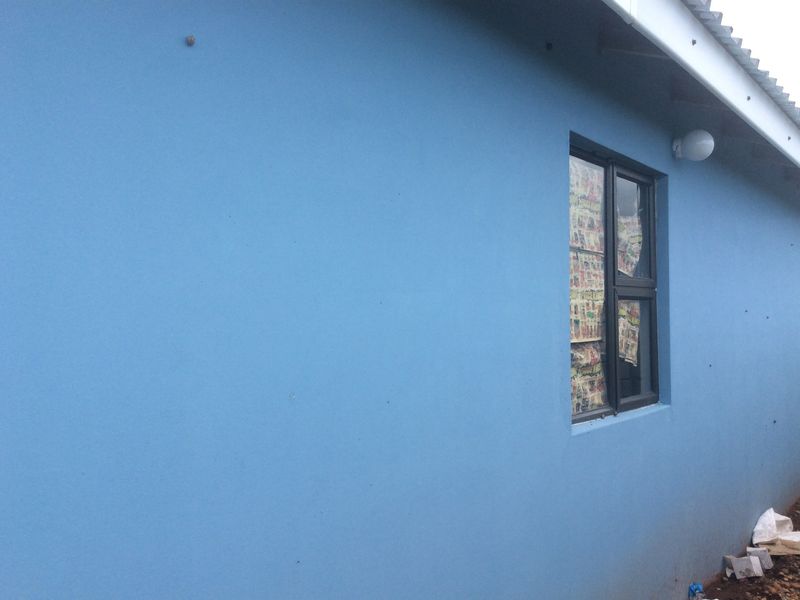 A view of the exterior rear wall featuring a blue painted finish, an aluminium window frame, and an exterior light fixture.
