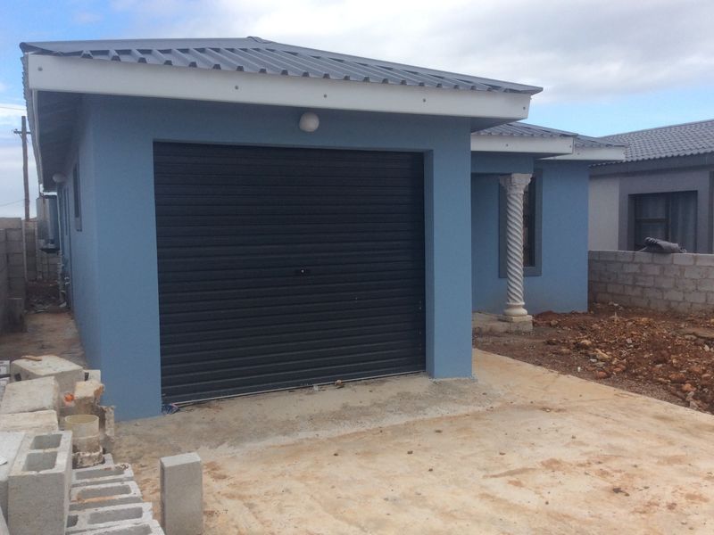 Front exterior view of a house featuring a roller garage door, decorative column, and unfinished driveway area.