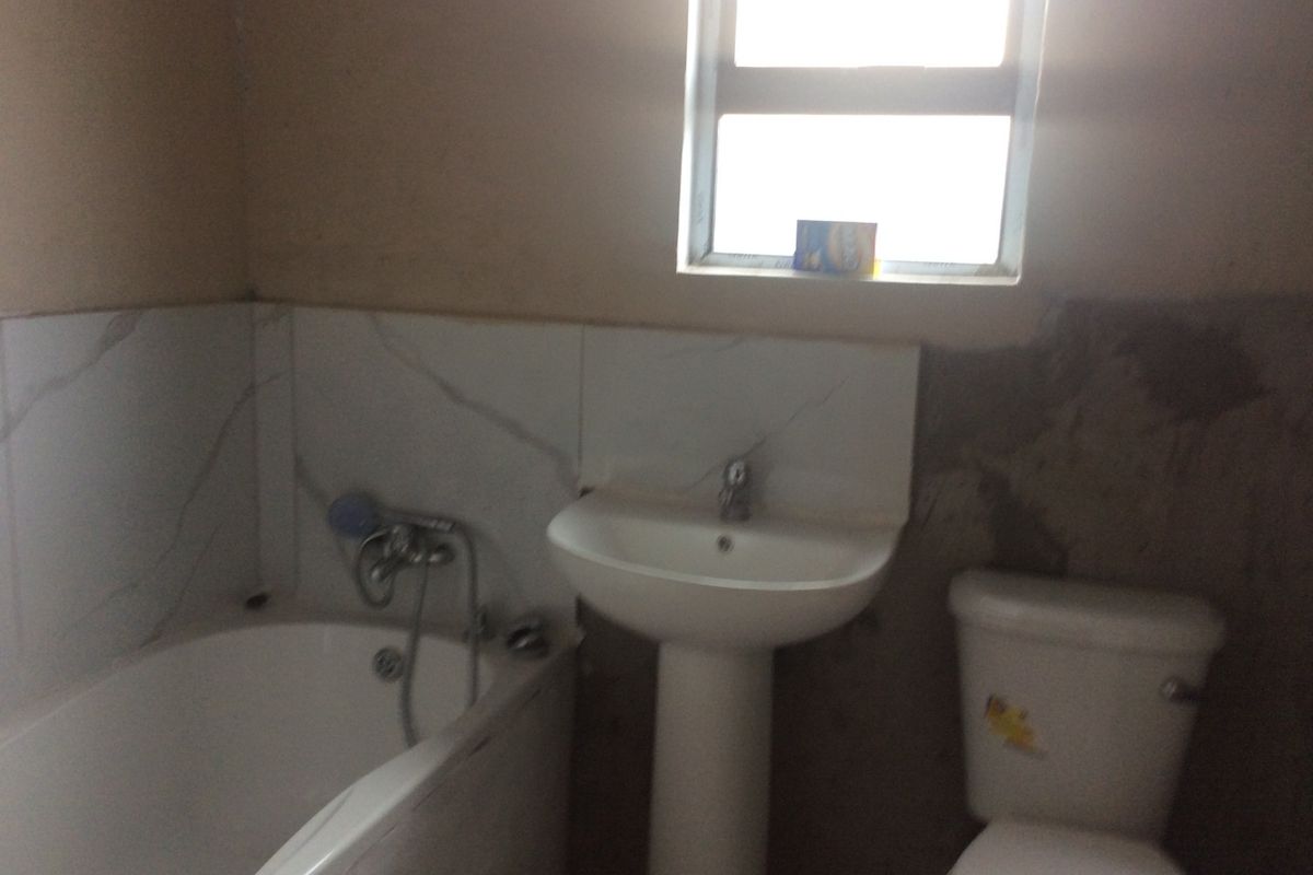 A bathroom featuring a bathtub, pedestal basin, and toilet, currently requiring completion of wall tiling and plastering work.