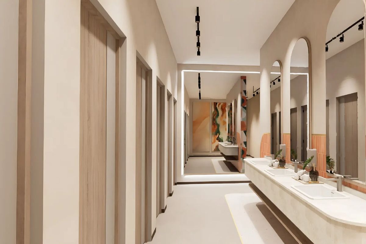 Modern office bathroom featuring a long integrated vanity with multiple sinks, arched mirrors, track lighting, and a clean, contemporary aesthetic.