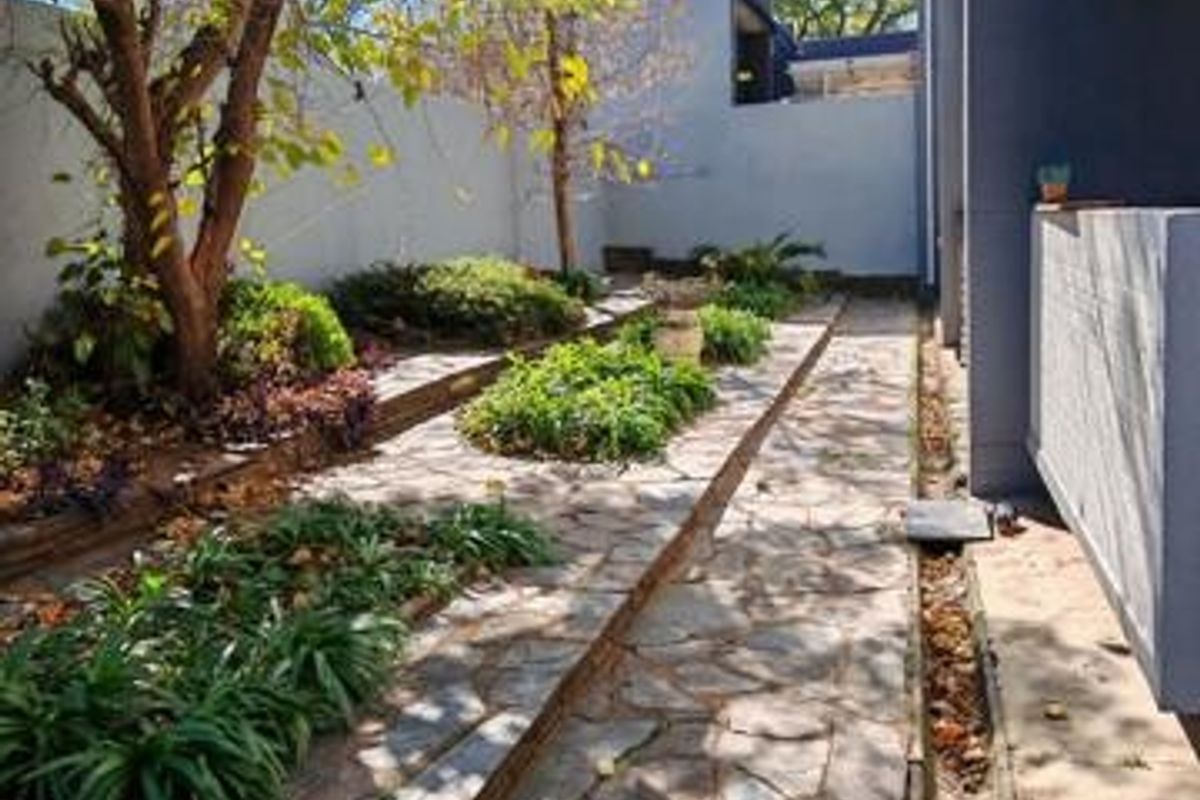 A rear garden area featuring a stone-paved pathway, landscaped garden beds, and a perimeter wall, providing a private outdoor space.