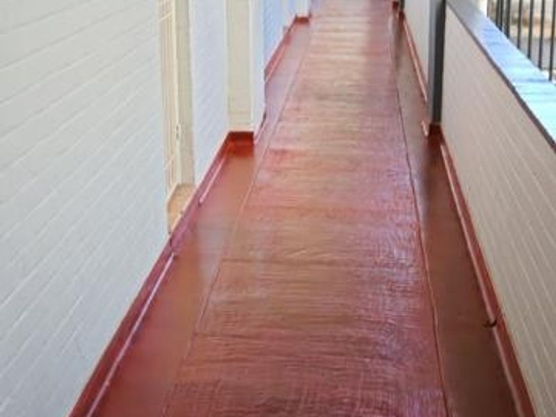 An exterior apartment hallway featuring painted brick walls, a metal security gate, and a painted concrete walkway with a safety railing.