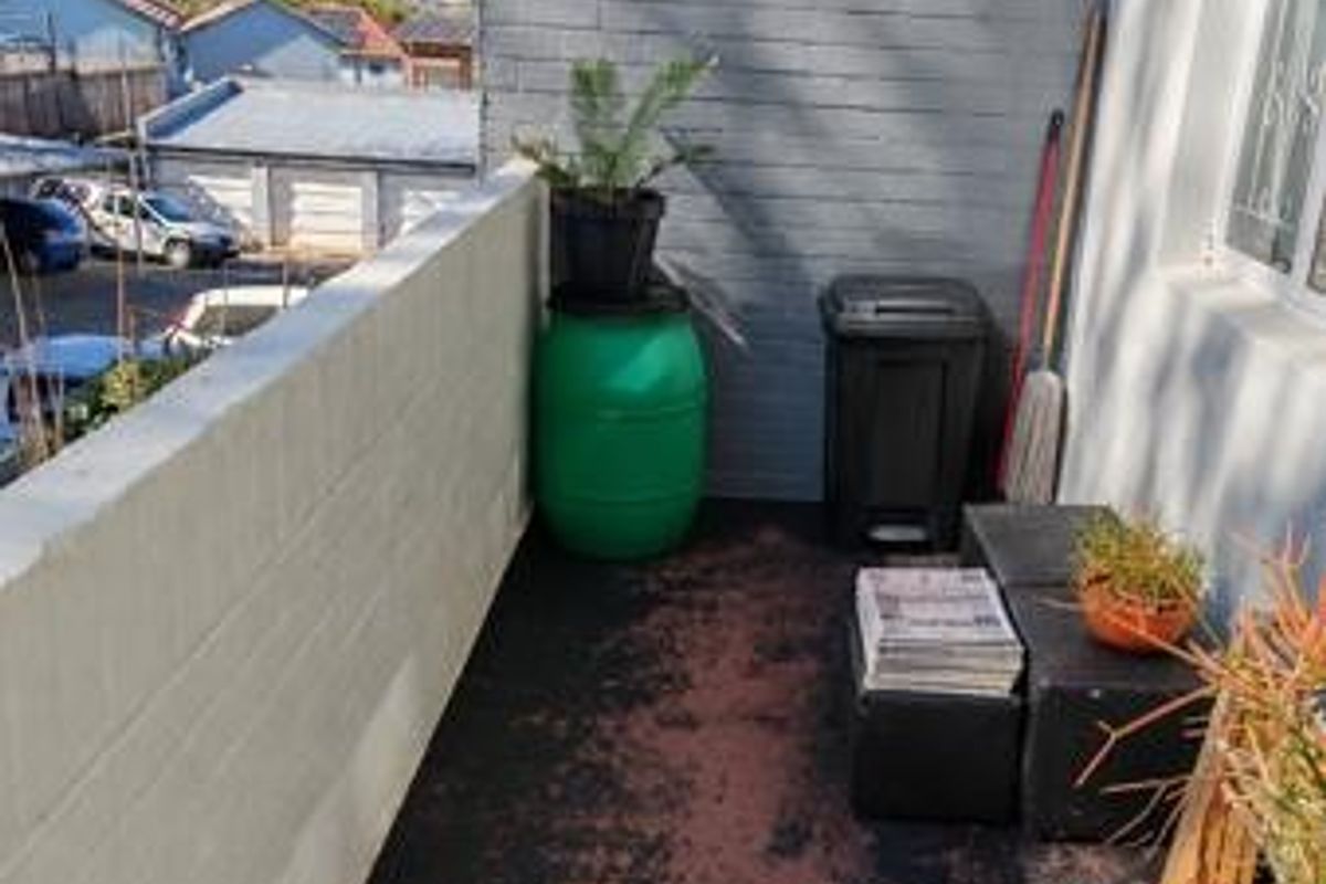 A compact balcony area featuring a painted brick wall and a worn floor surface, offering an outdoor space with views of the surrounding neighborhood.