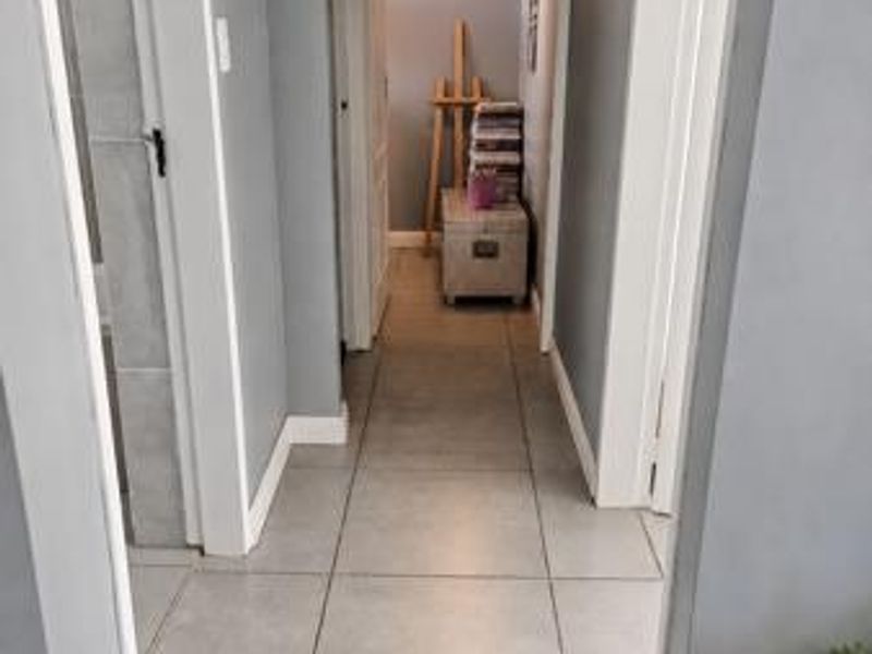 A clean and well-maintained hallway featuring neutral tiled flooring and white door frames, providing access to multiple rooms within the apartment.