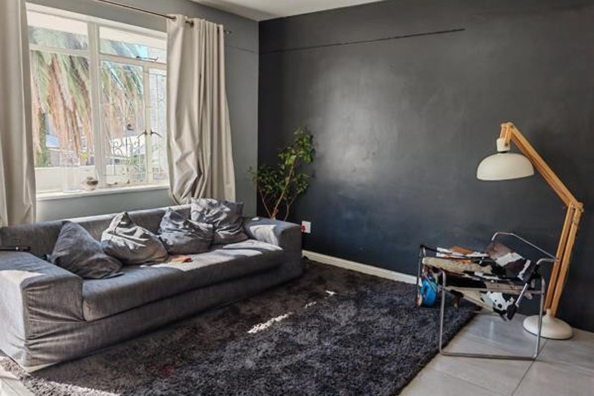 A living room featuring tiled flooring and a large window with security bars, accented by a dark feature wall.