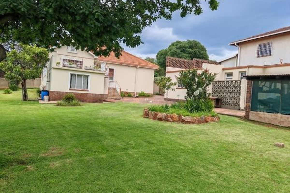Spacious rear garden featuring a well-maintained lawn, established garden beds, and views of the property's rear facade and outbuildings.