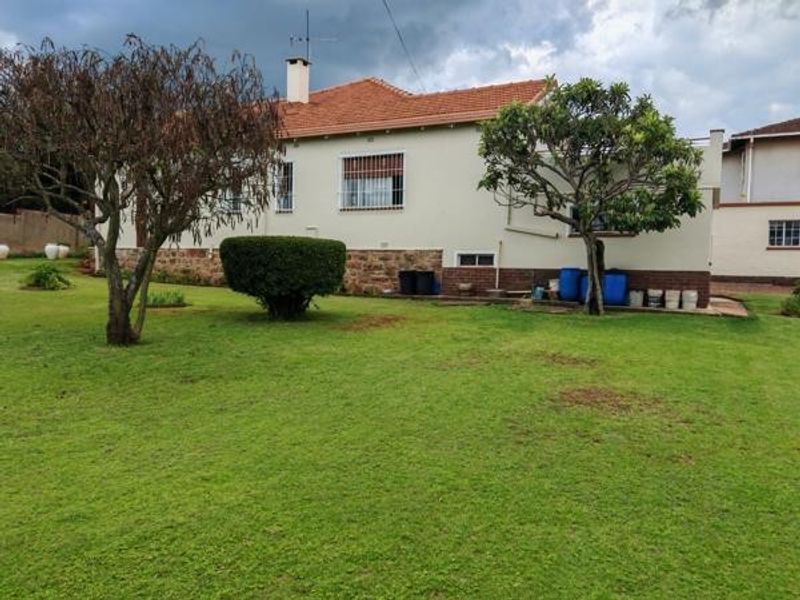 Rear view of the house featuring a spacious lawn, terracotta tiled roof, and stone cladding base with security-fitted windows.