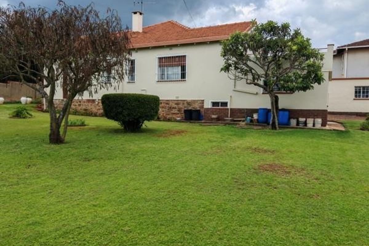 Rear view of the house featuring a spacious lawn, terracotta tiled roof, and stone cladding base with security-fitted windows.