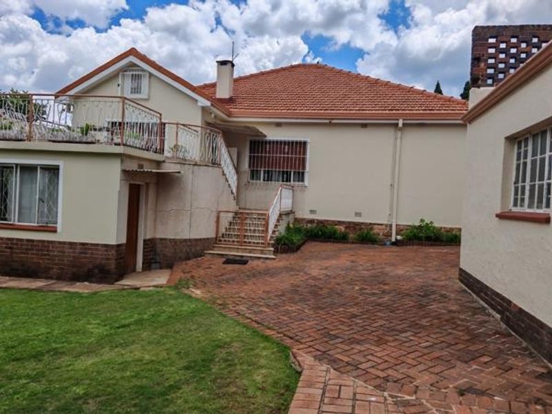 Rear view of the property featuring a terracotta tiled roof, brick paved courtyard, and an elevated balcony with wrought iron railings.
