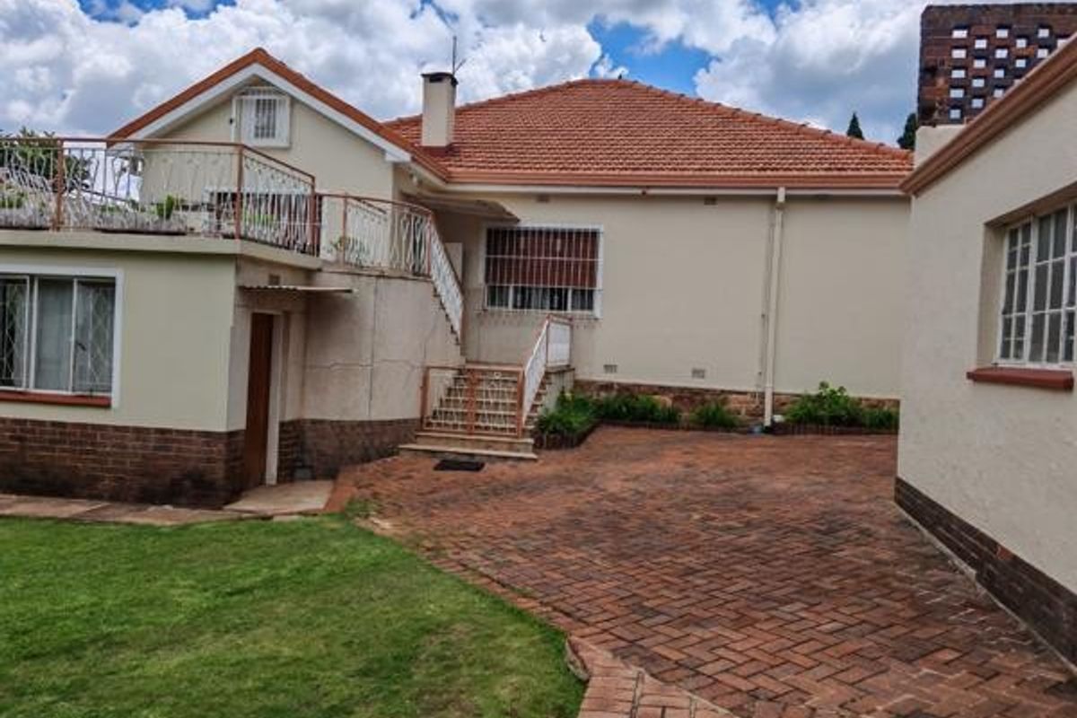 Rear view of the property featuring a terracotta tiled roof, brick paved courtyard, and an elevated balcony with wrought iron railings.
