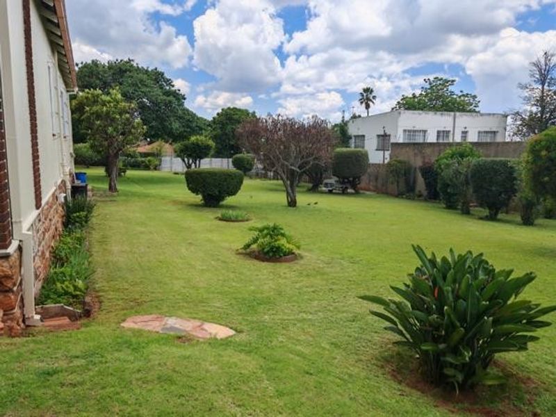 A spacious, well-maintained garden featuring a large lawn, mature trees, established shrubs, and a stone pathway along the side of the house.