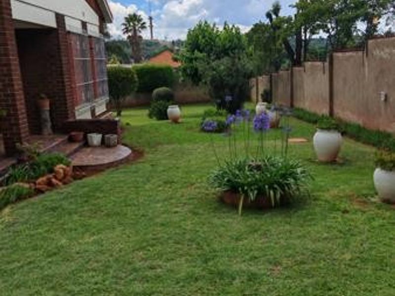 A well-maintained residential garden featuring a lush lawn, perimeter boundary wall, and a paved patio area adjacent to the brick-built house.