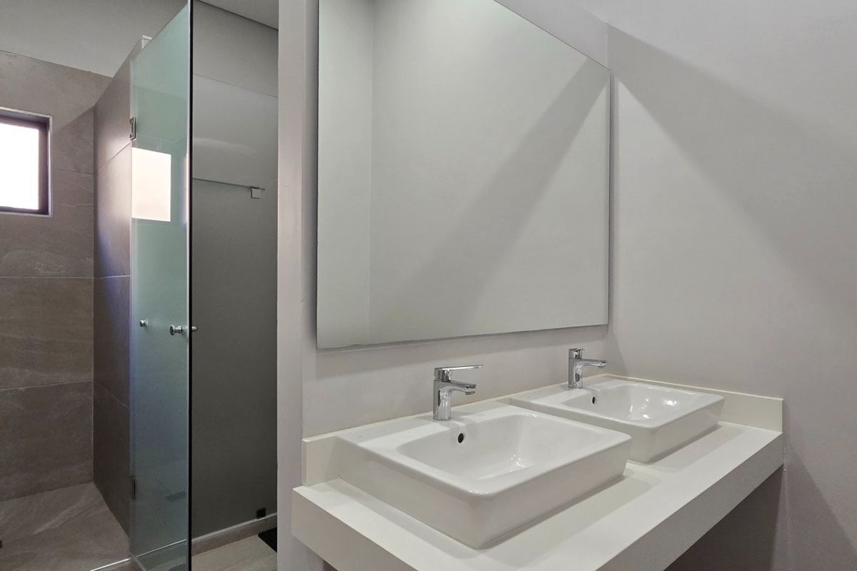 Modern bathroom featuring a double vanity with vessel sinks, a large wall mirror, and a spacious walk-in shower with a glass enclosure.