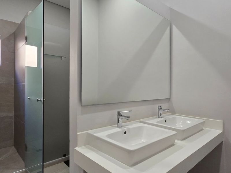 Modern bathroom featuring a double vanity with vessel sinks, a large wall mirror, and a spacious walk-in shower with a glass enclosure.