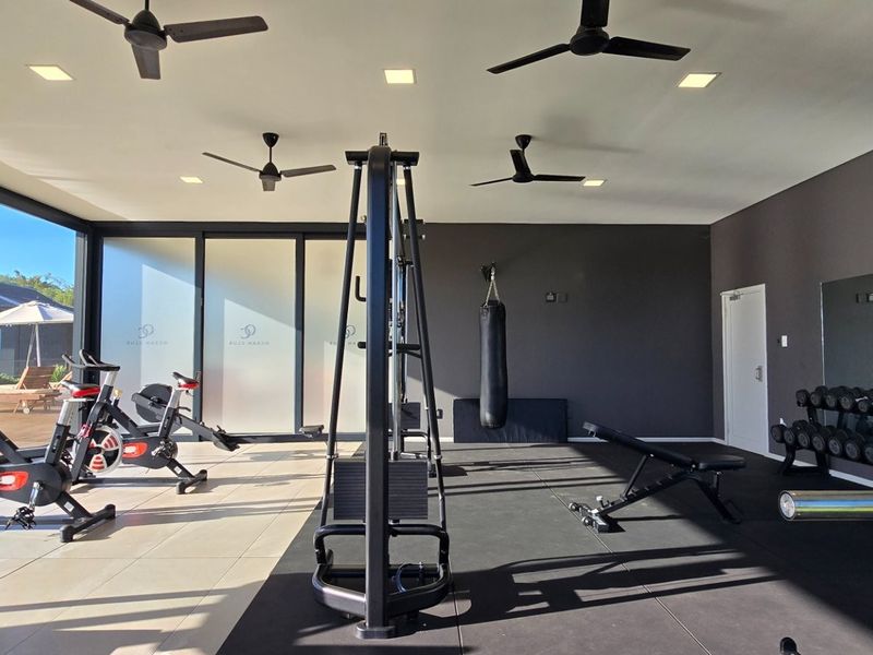 A modern, well-equipped home gym featuring large sliding glass doors, recessed lighting, ceiling fans, and a large wall mirror.