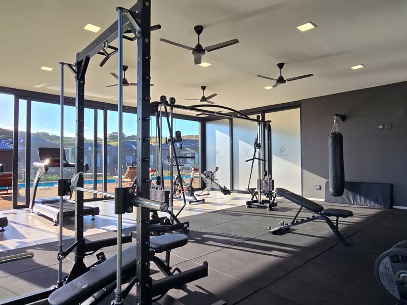 Modern home gym featuring rubber flooring, recessed lighting, ceiling fans, and large sliding glass doors providing seamless access to the outdoor pool area.
