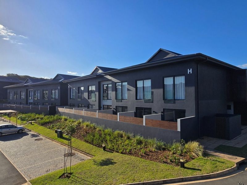 A modern multi-unit residential complex featuring dark exterior finishes, paved parking areas, and landscaped garden beds with timber privacy screens.