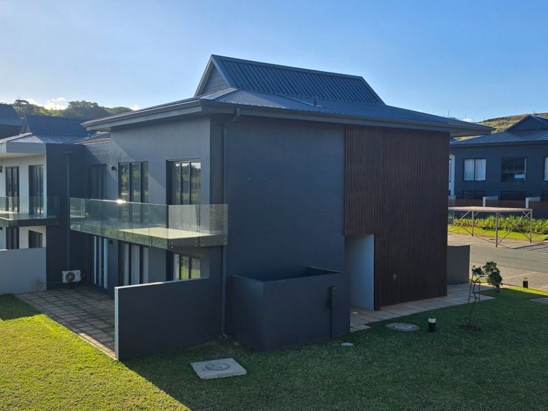 Rear view of a modern double-story townhouse featuring dark exterior finishes, timber cladding accents, glass balconies, and a private paved patio area.