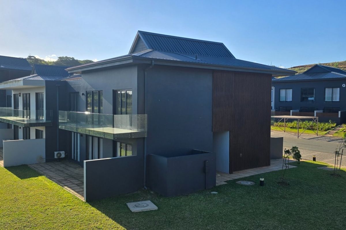 Rear view of a modern double-story townhouse featuring dark exterior finishes, timber cladding accents, glass balconies, and a private paved patio area.