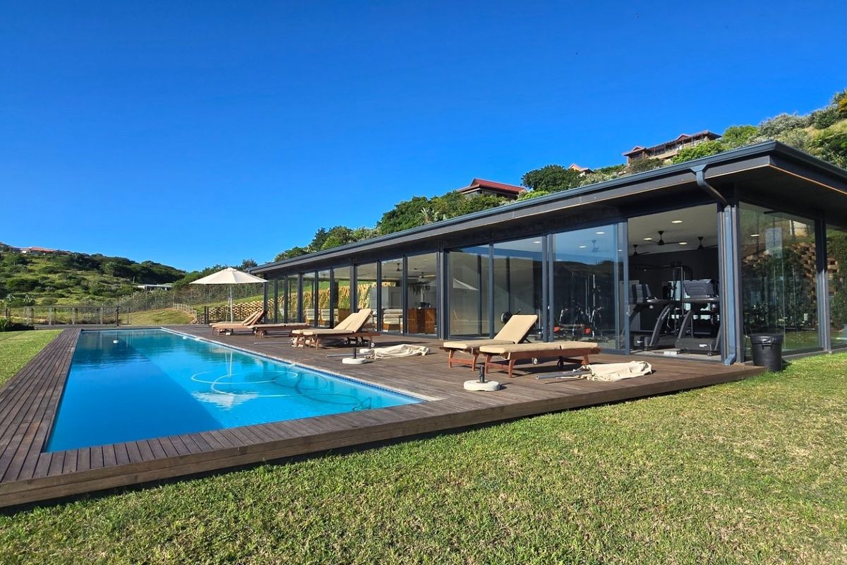 Modern outdoor living area featuring a sleek swimming pool, expansive timber decking, and large glass sliding doors connecting to the interior gym space.