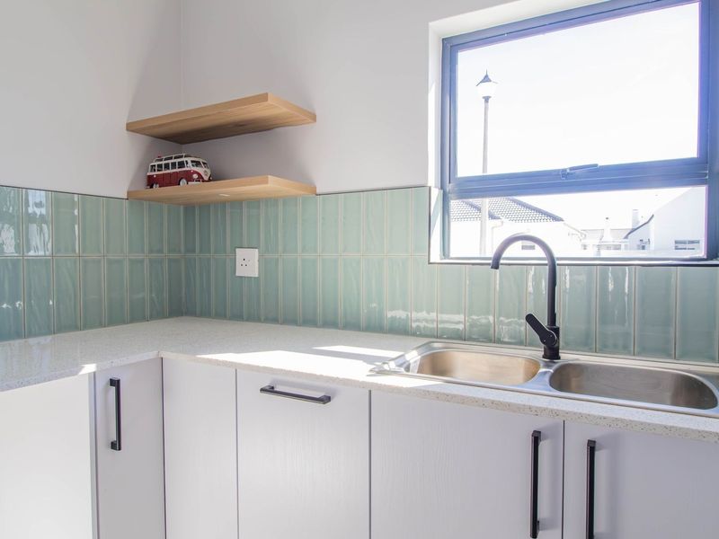 Modern kitchen area featuring a double sink, black mixer tap, stone countertops, and stylish light green subway tile backsplash with floating shelving.