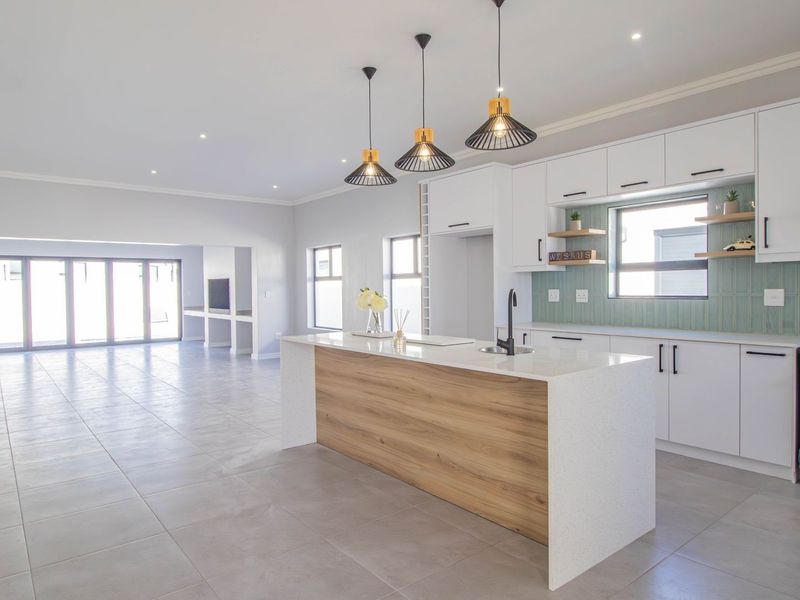 Modern open-plan kitchen and living area featuring a central island, quartz countertops, sleek white cabinetry, and contemporary pendant lighting with neutral tiled flooring throughout.