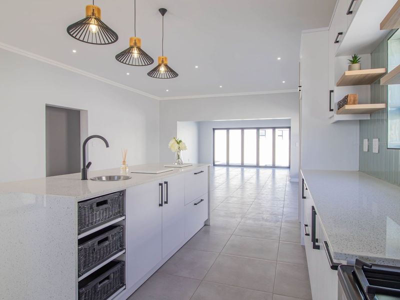 Modern open-plan kitchen featuring a central island with quartz countertops, sleek cabinetry, floating shelves, and large stacking doors leading to the outdoor area.