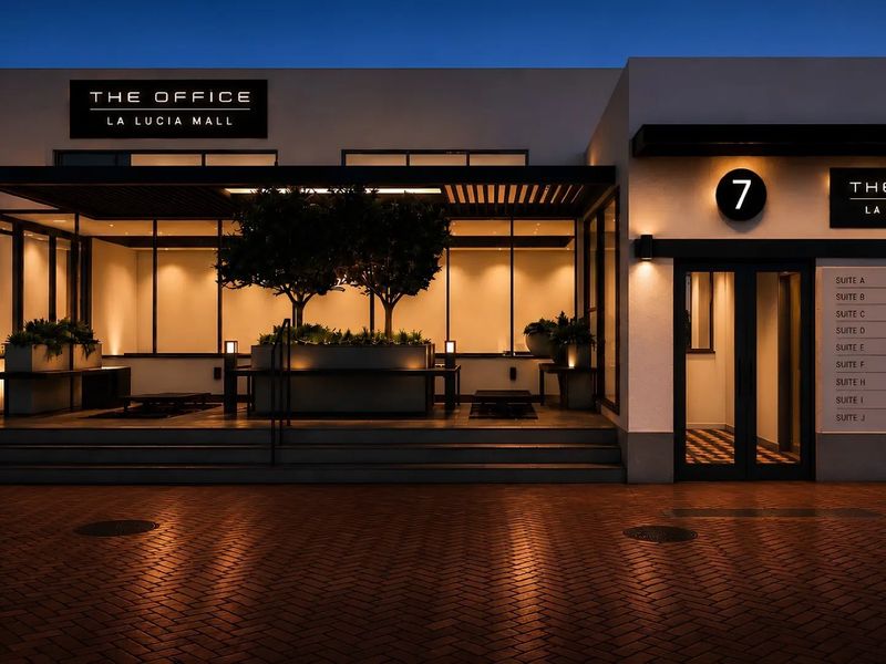 Modern office building entrance at La Lucia Mall featuring a well-lit glass facade, professional signage, and paved exterior approach.