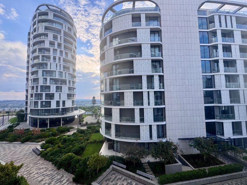 A view of modern high-rise apartment towers featuring glass balconies and landscaped grounds with paved walkways.