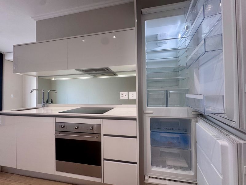 Modern kitchen featuring sleek white cabinetry, integrated appliances, stone countertops, and a reflective mirror splashback.