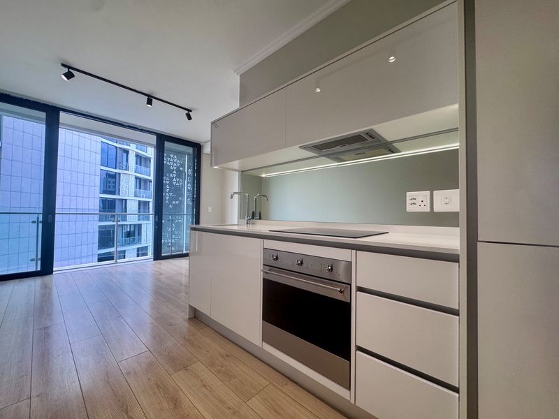 Modern kitchen featuring sleek white cabinetry, integrated appliances, mirrored splashback, and laminate flooring, seamlessly connected to a balcony with urban views.