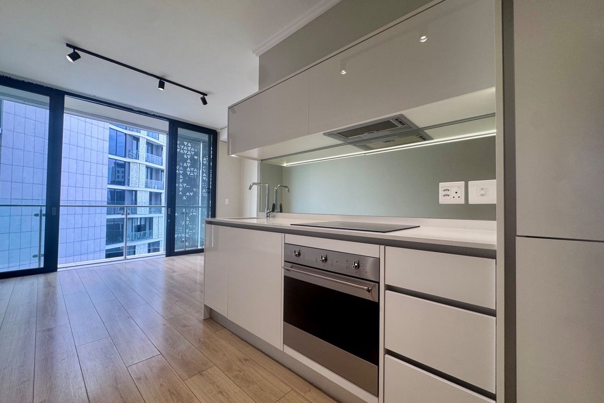 Modern kitchen featuring sleek white cabinetry, integrated appliances, mirrored splashback, and laminate flooring, seamlessly connected to a balcony with urban views.