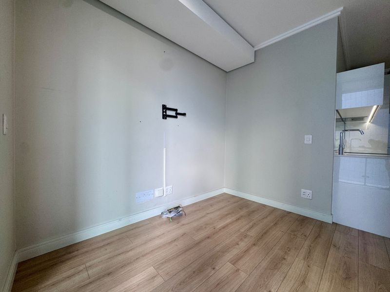 An empty open-plan living area featuring laminate flooring, a wall-mounted TV bracket, and an adjacent modern kitchen with built-in cabinetry.