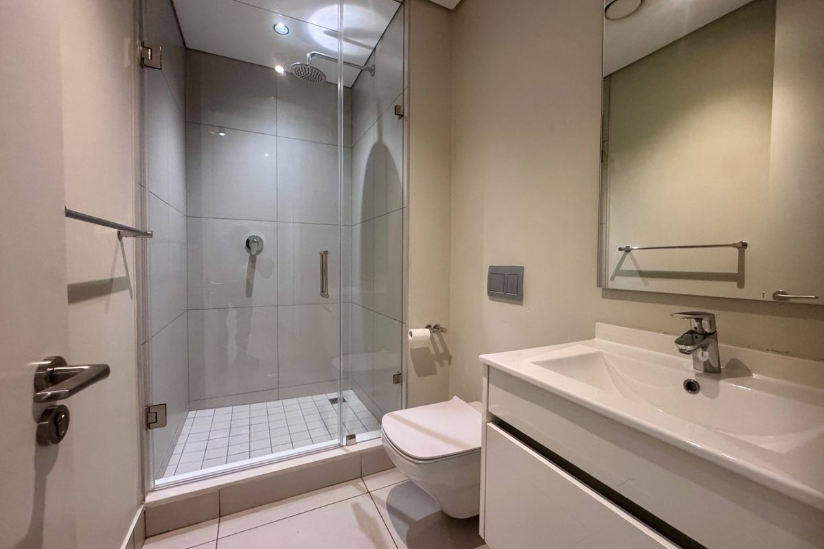 A modern, well-maintained bathroom featuring a glass-enclosed shower, wall-mounted toilet, and a sleek vanity with an integrated basin.