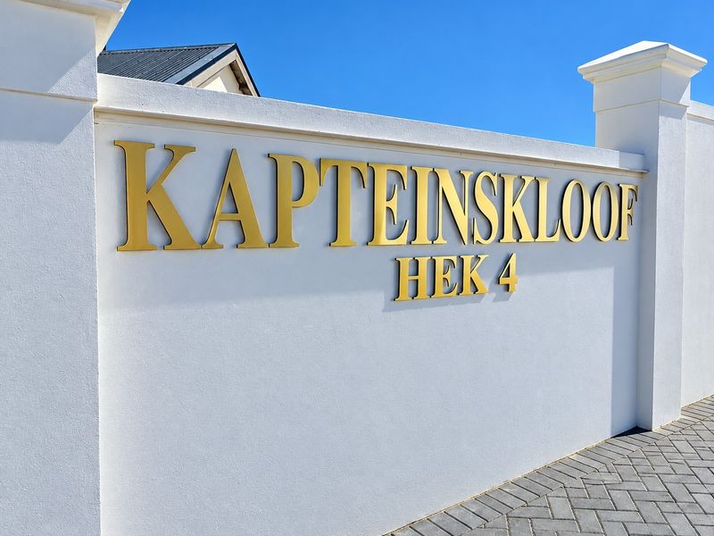 A clean, modern boundary wall featuring gold signage for Kapteinskloof Hek 4, set against a clear blue sky with paved driveway access.