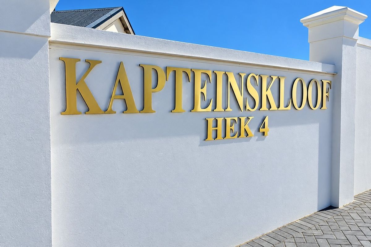 A clean, modern boundary wall featuring gold signage for Kapteinskloof Hek 4, set against a clear blue sky with paved driveway access.