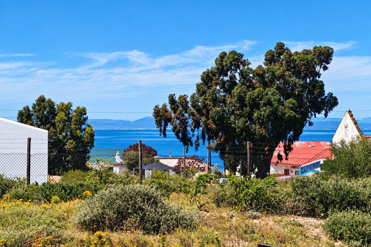 A scenic view of the ocean and distant mountains captured from the vacant residential land, featuring mature trees and surrounding neighborhood structures.