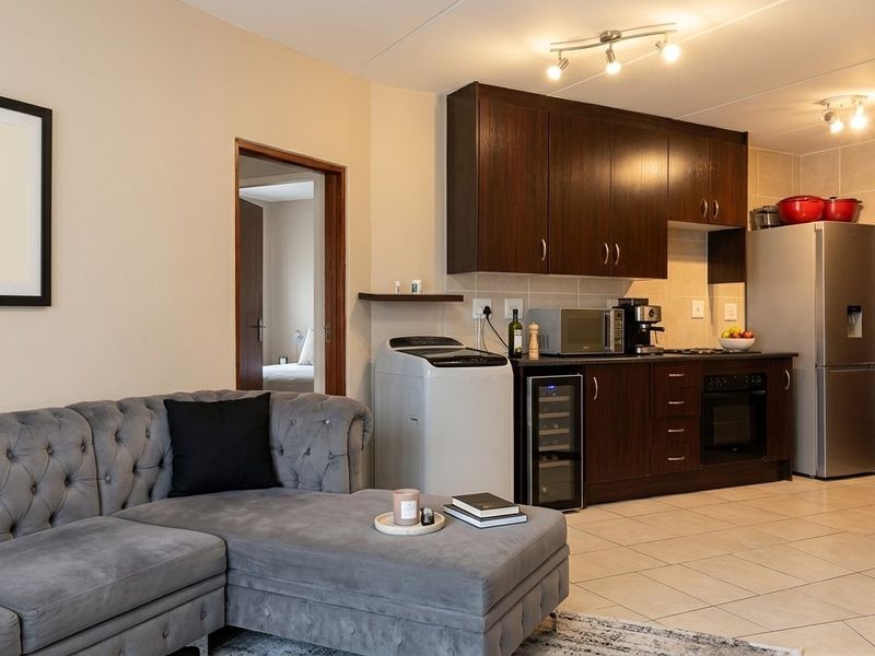 An open-plan living area featuring a modern kitchen with dark wood cabinetry, built-in appliances, tiled flooring, and an integrated air conditioning unit.