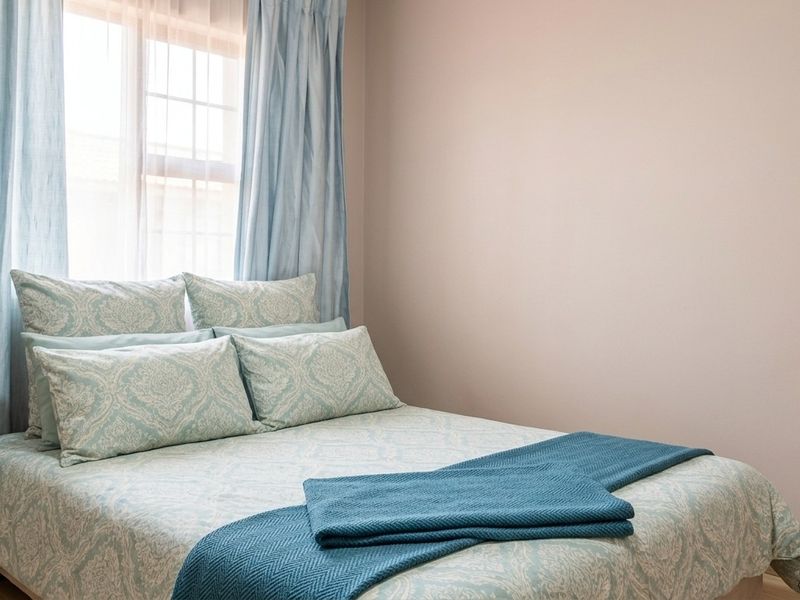 A well-lit bedroom featuring neutral wall finishes, laminate flooring, and a large window allowing for natural light.