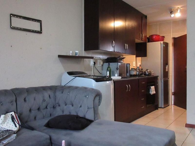 Open plan living area featuring a compact kitchen with dark wood cabinetry, tiled flooring, and integrated appliances, suitable for modern apartment living.