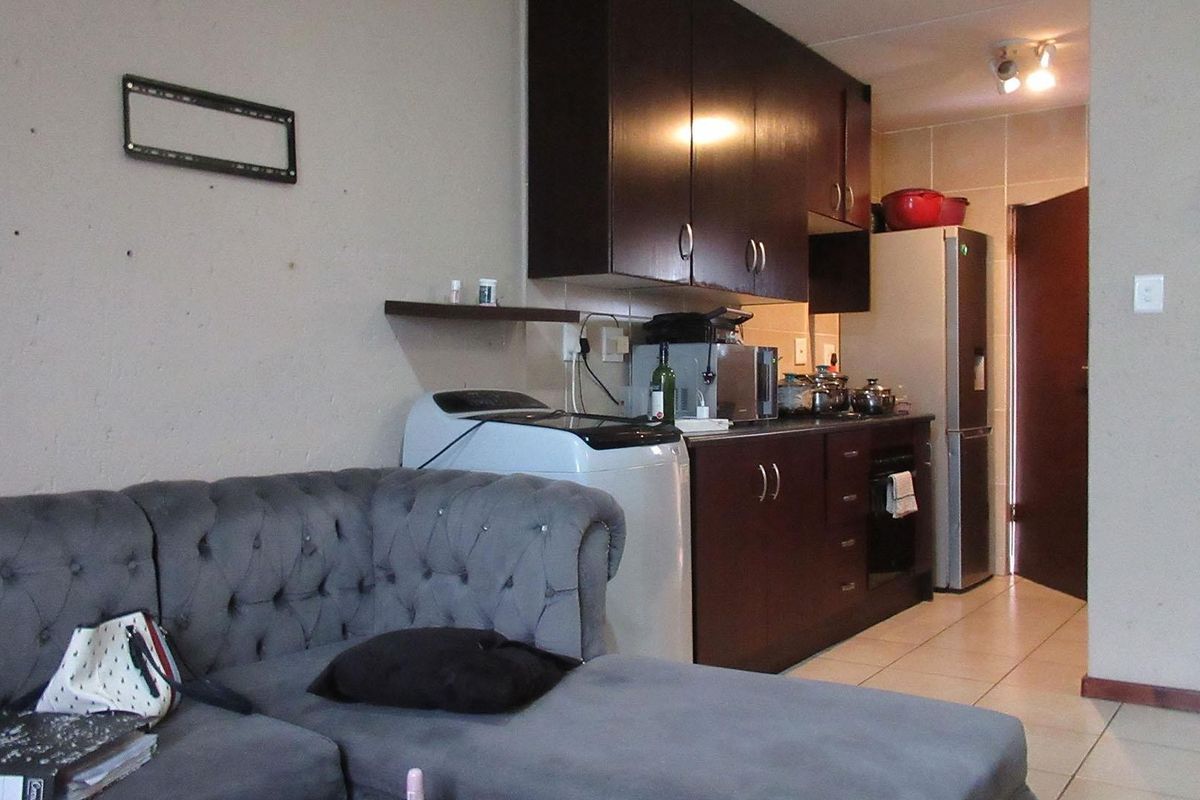 Open plan living area featuring a compact kitchen with dark wood cabinetry, tiled flooring, and integrated appliances, suitable for modern apartment living.