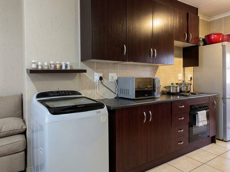A functional kitchen featuring dark wood cabinetry, a built-in oven with hob, tiled backsplash, and tiled flooring, providing a practical workspace.