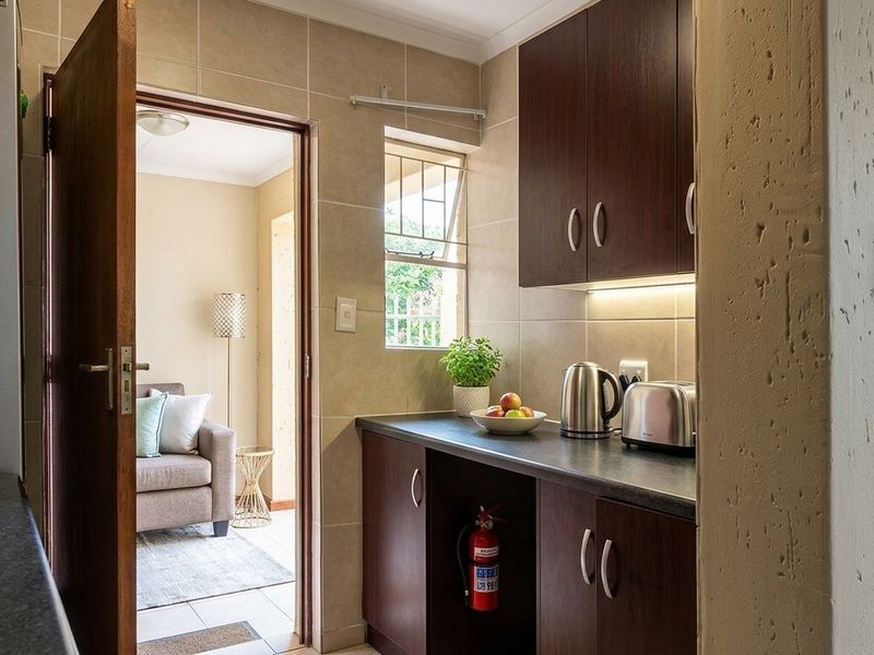 A compact scullery area featuring dark wood cabinetry, laminate countertops, and tiled walls, providing functional prep space adjacent to the main living area.