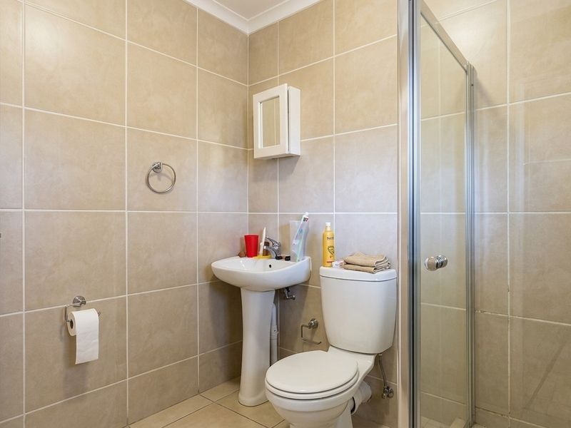 A functional bathroom featuring a pedestal sink, toilet, and a glass-enclosed shower with neutral wall and floor tiling.