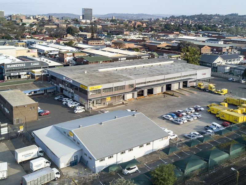 Aerial view of a commercial industrial facility featuring large warehouse buildings, loading bays, extensive parking, and a paved yard area in an urban setting.