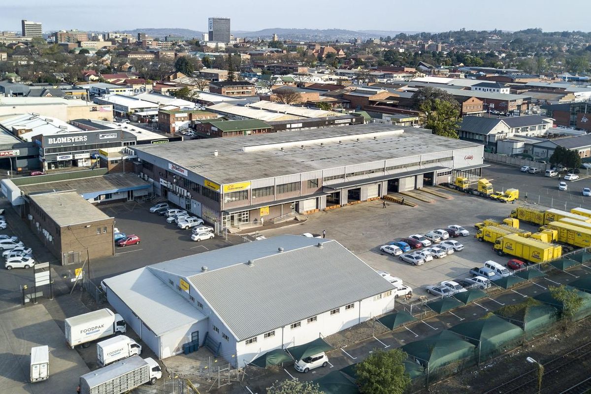 Aerial view of a commercial industrial facility featuring large warehouse buildings, loading bays, extensive parking, and a paved yard area in an urban setting.