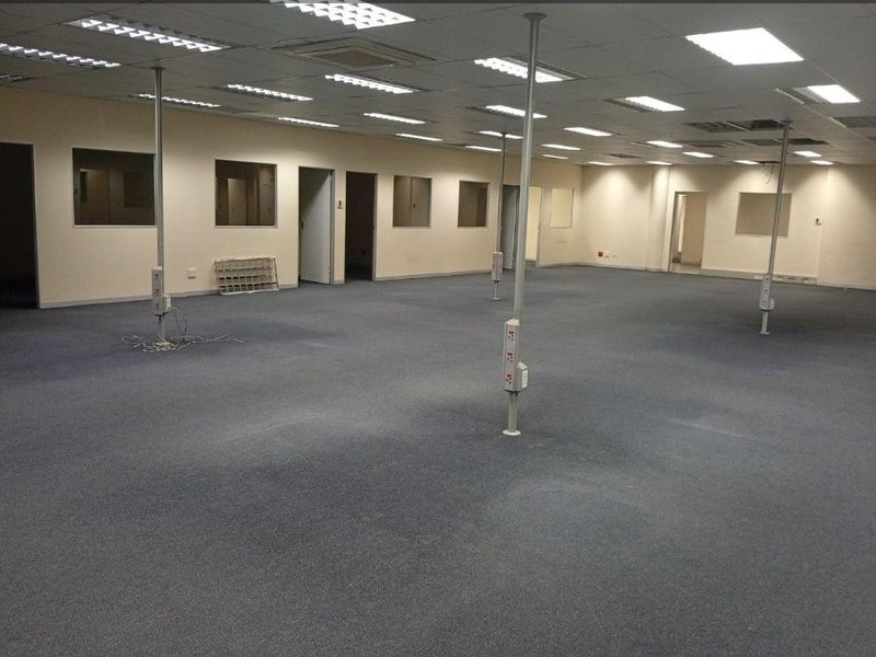 Spacious open-plan commercial office area featuring suspended ceilings, recessed lighting, and multiple structural support columns with integrated electrical power points.