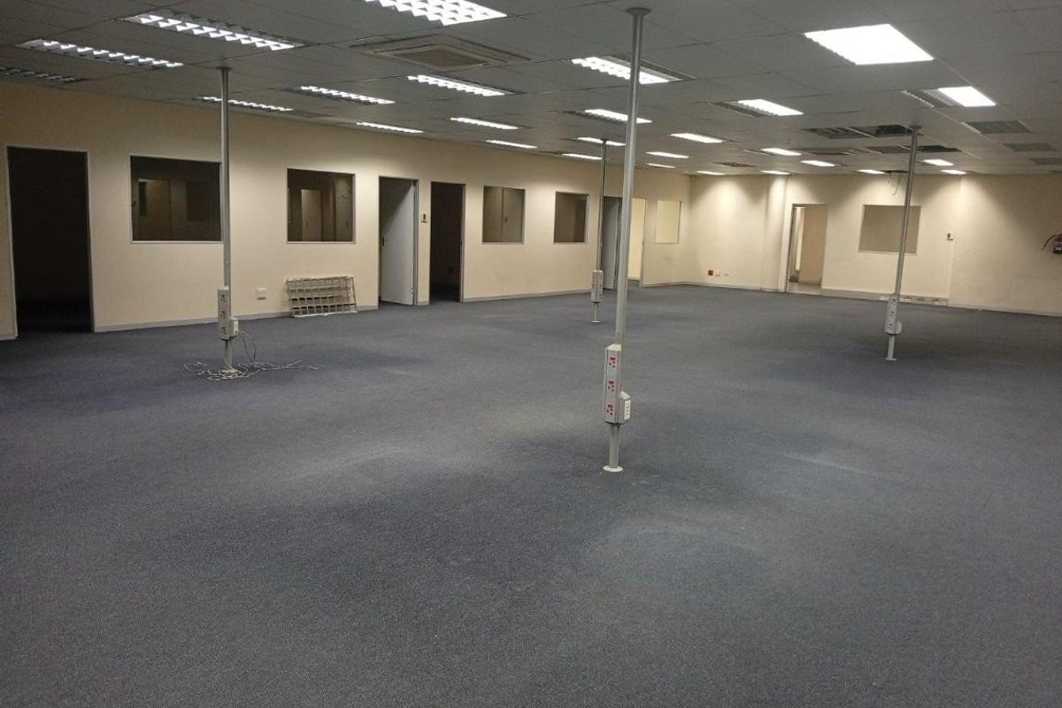 Spacious open-plan commercial office area featuring suspended ceilings, recessed lighting, and multiple structural support columns with integrated electrical power points.