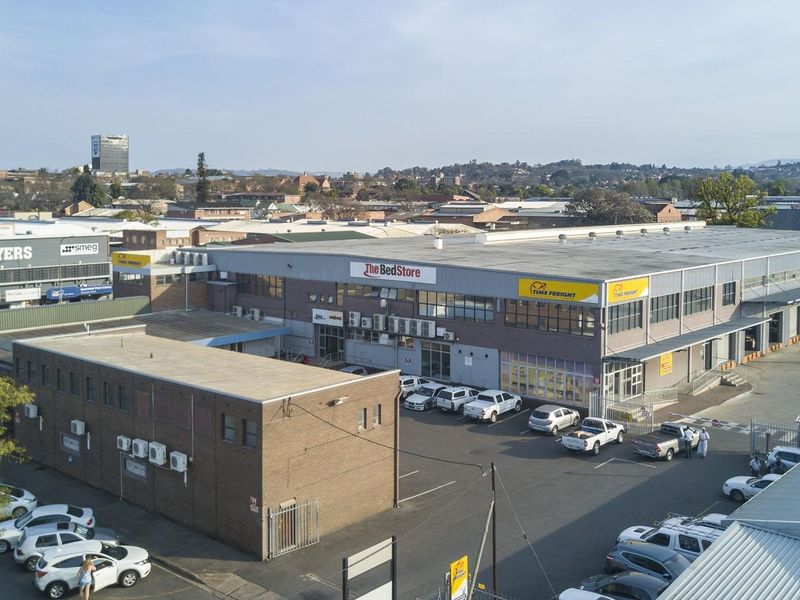 Aerial view of a commercial warehouse complex featuring brick construction, metal roofing, external air conditioning units, and an asphalt parking area.