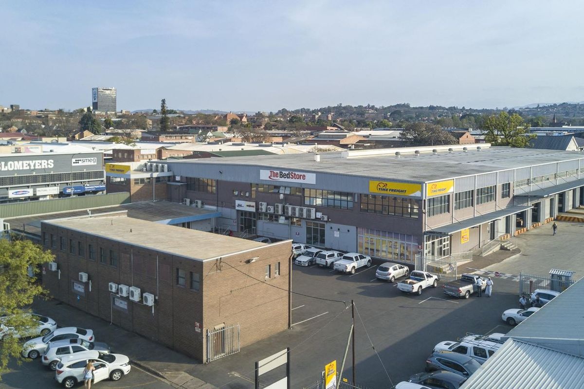 Aerial view of a commercial warehouse complex featuring brick construction, metal roofing, external air conditioning units, and an asphalt parking area.